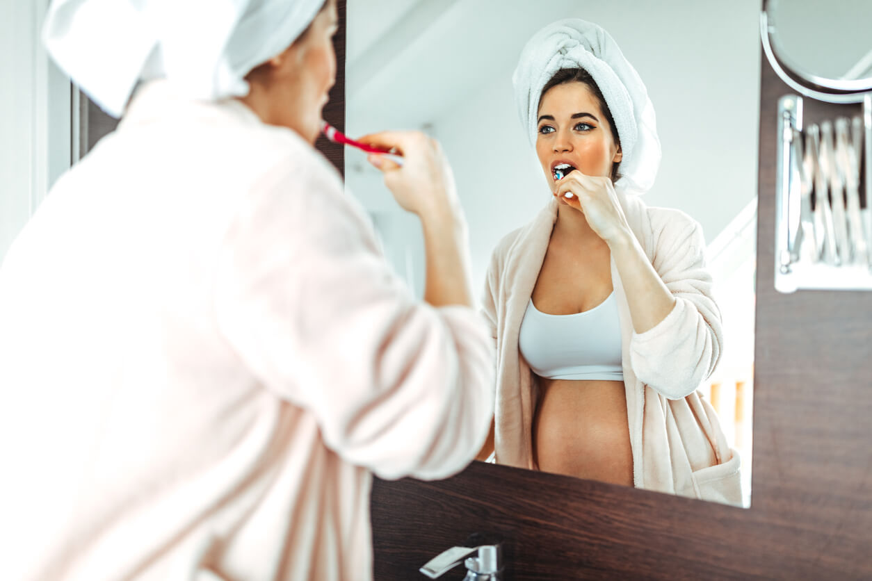 A pregnant woman brushing her teeth in the mirror.