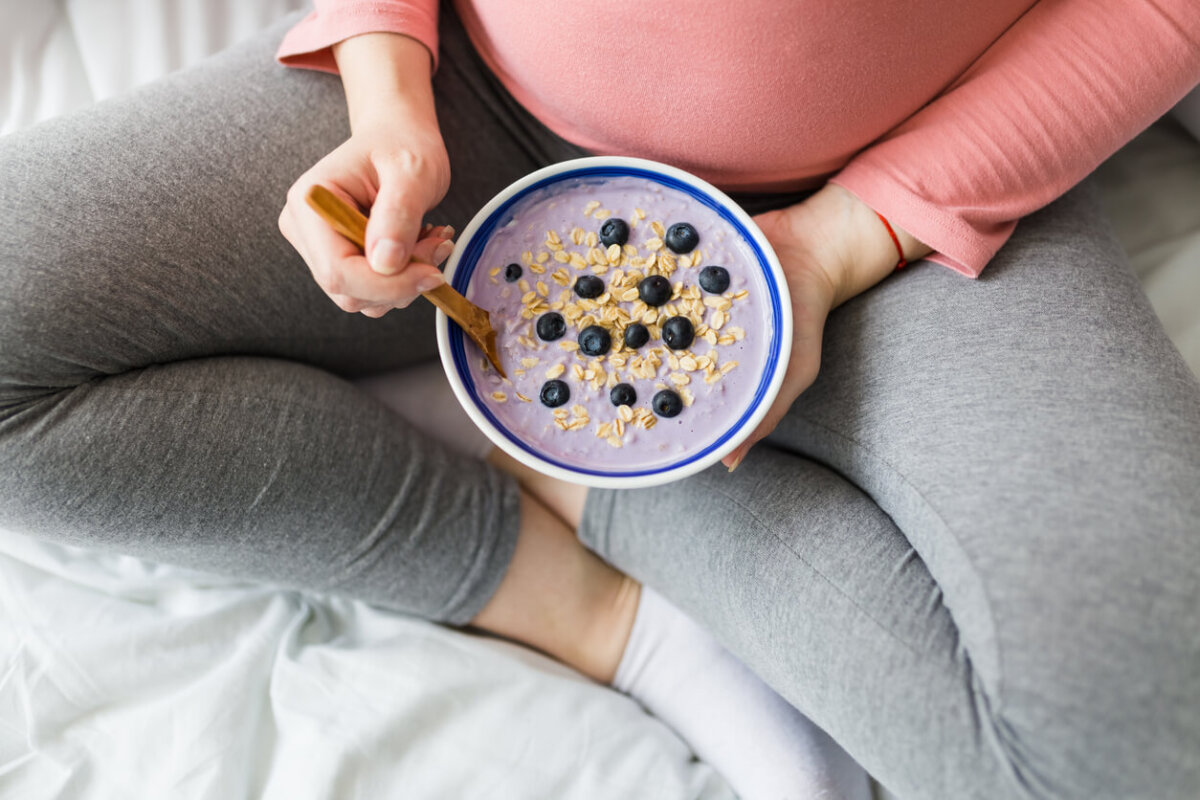 Mujer embarazada comiendo yogur con cereales y fruta.