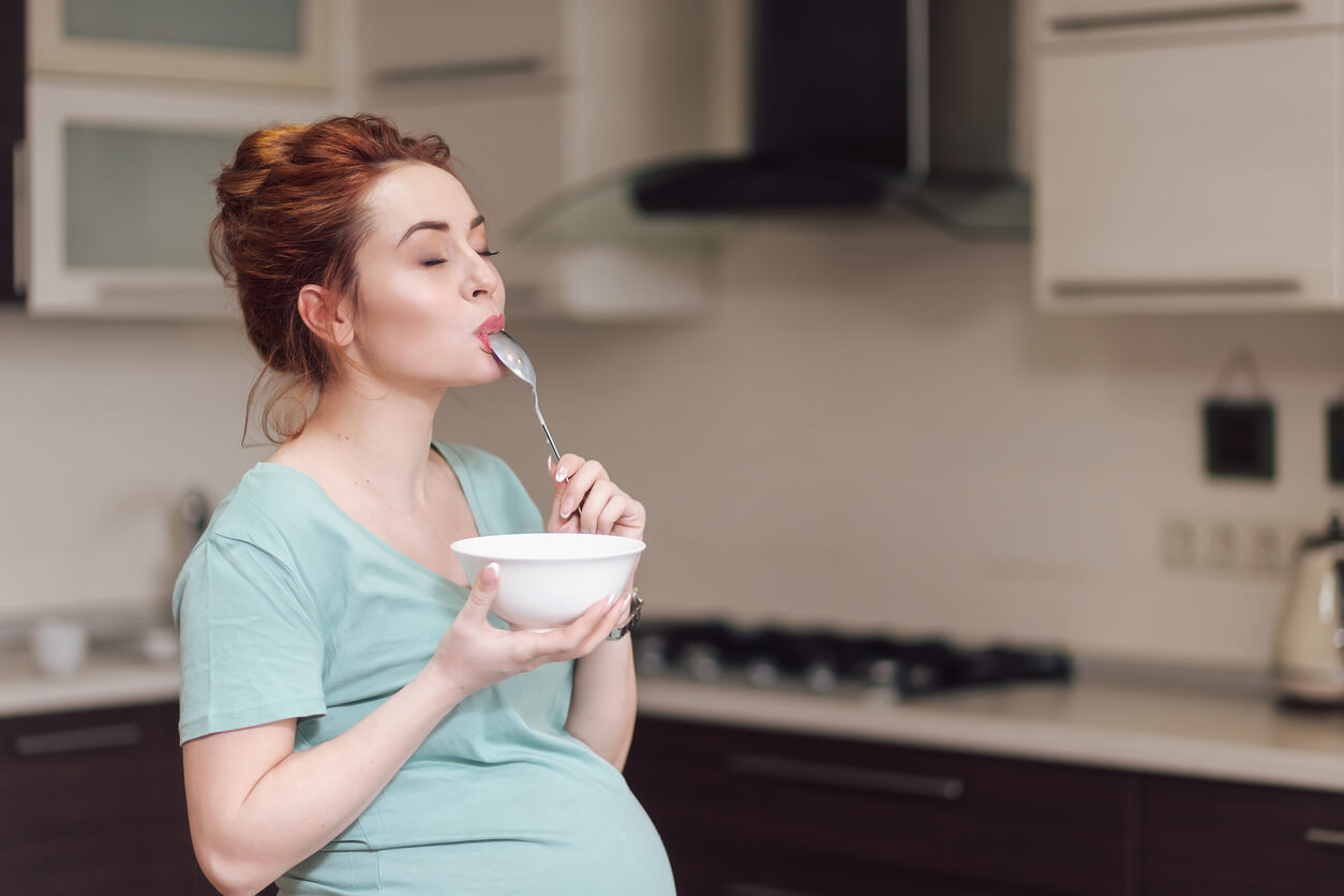 Mujer embarazada disfrutando mientras come durante el tercer trimestre del embarazo.