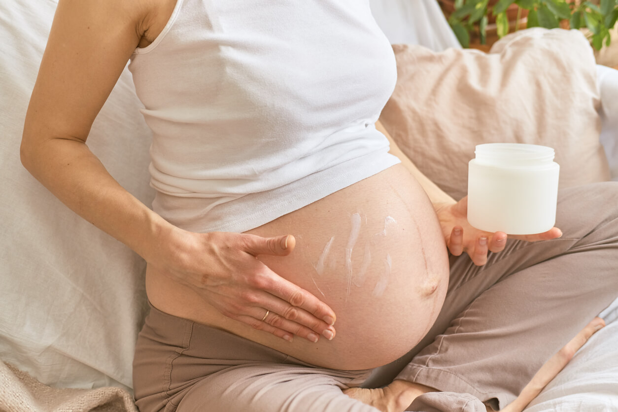 Mulher grávida fazendo massagem e aplicando creme para reduzir o aparecimento de estrias.