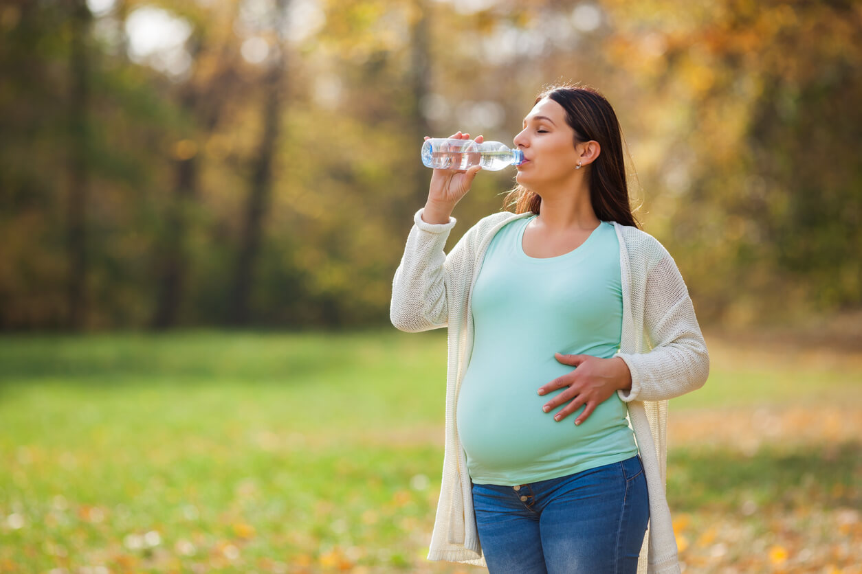 Mujer embarazada en un parque bebiendo agua.