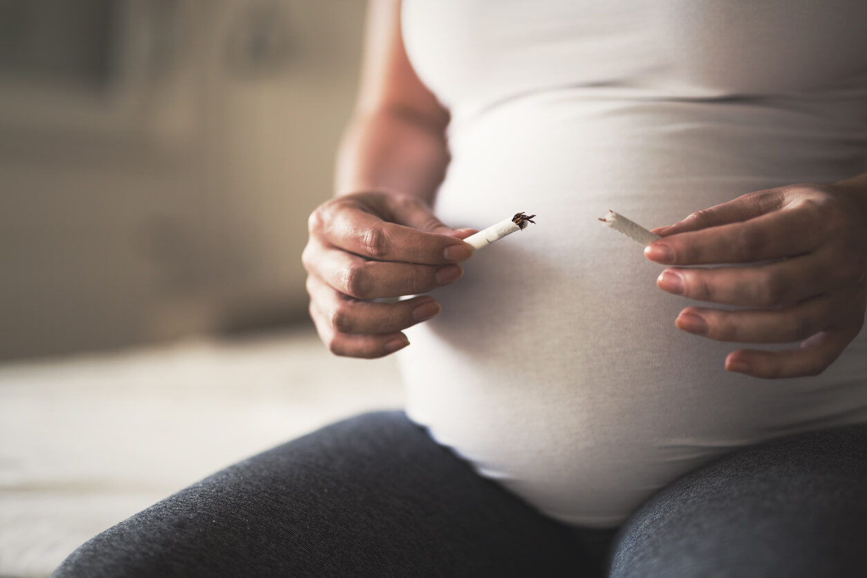 Mujer embarazada rompiendo un cigarrillo porque saber lo peligroso que es fumar durante el embarazo.