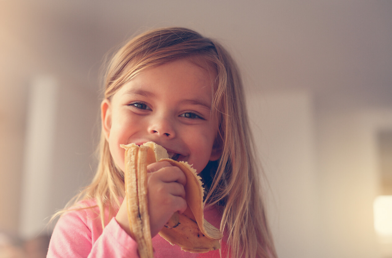 Niña feliz comiendo un plátano.