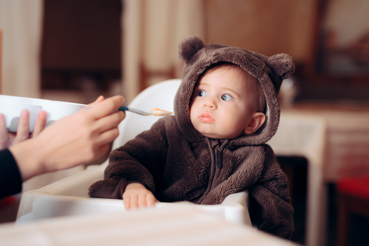 A baby girl who's moving away from the spoon of food her mother's offering her.