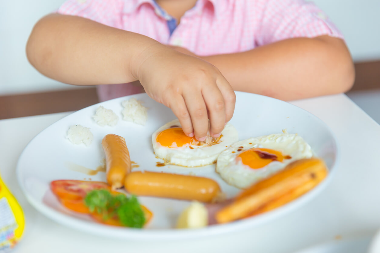 Niño comiendo huevos con salchichas.