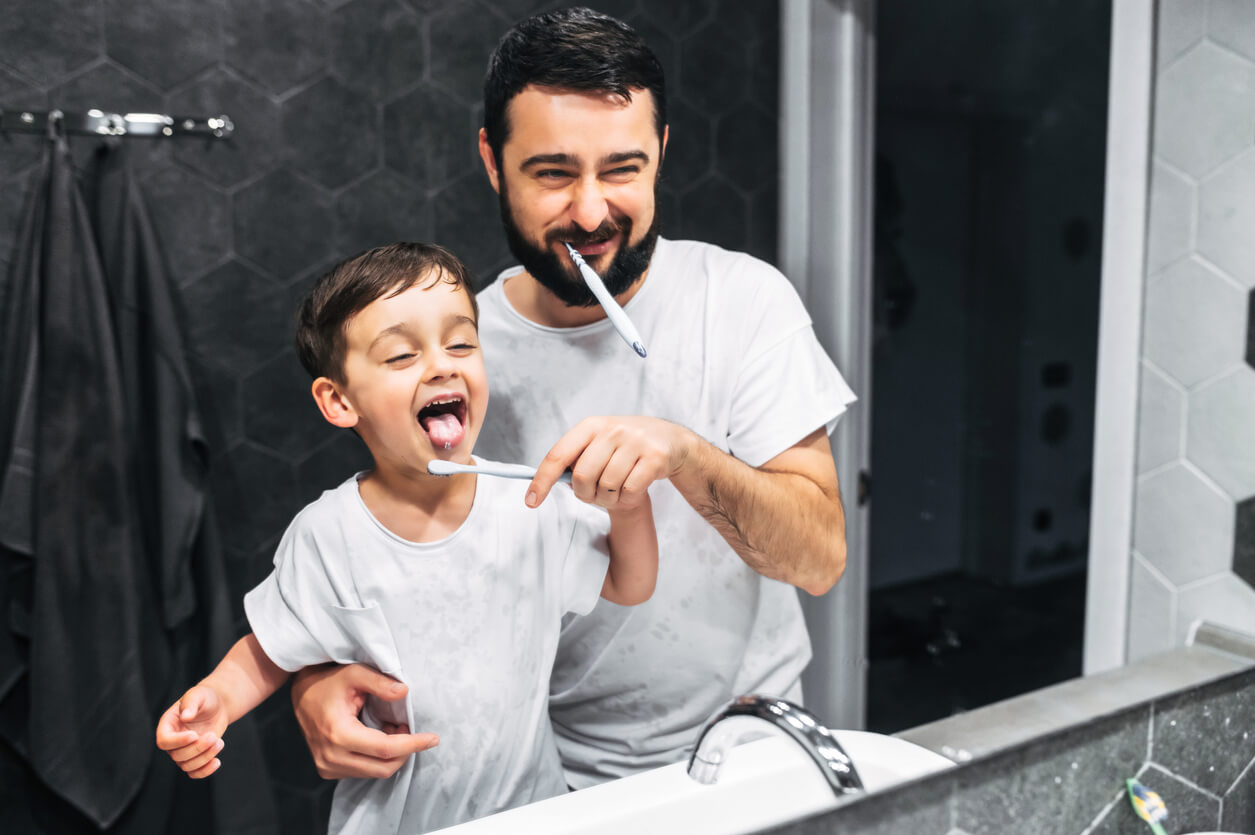 Padre e hijo lavándose los dientes frente al espejo.