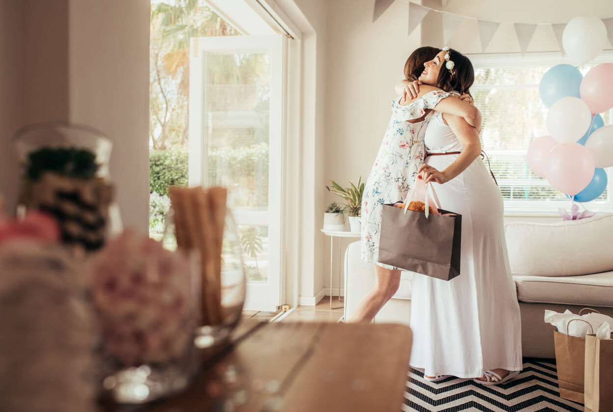 Amiga dando un abrazo a la futura mamá en el baby shower..