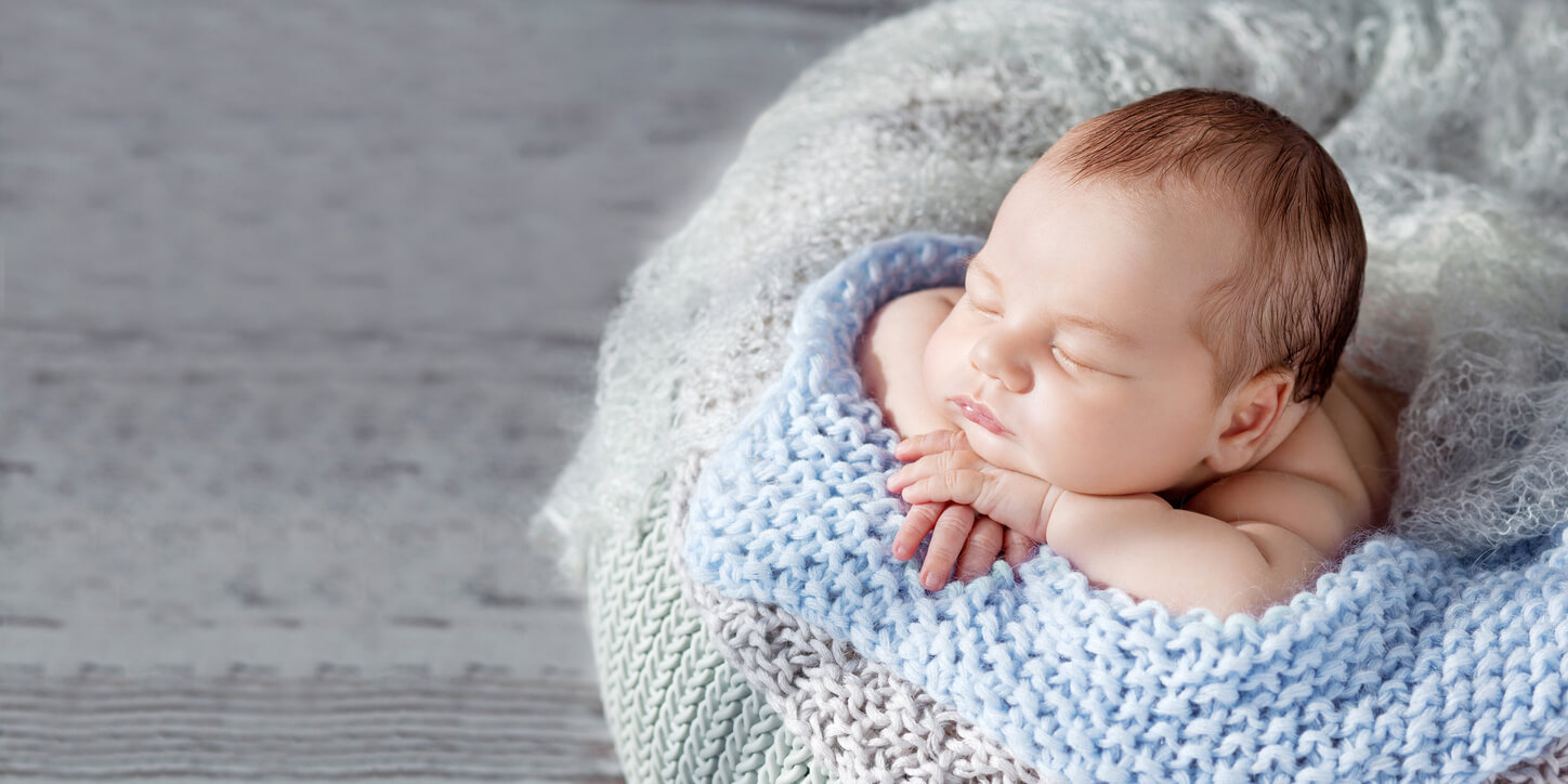 A baby boy lying on a knit blanket.