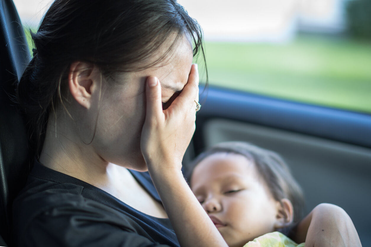 Madre triste llorando en el coche con su hijo en brazos.