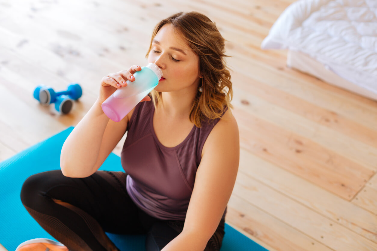 Mulher bebendo água após uma sessão de exercícios no pós-parto.
