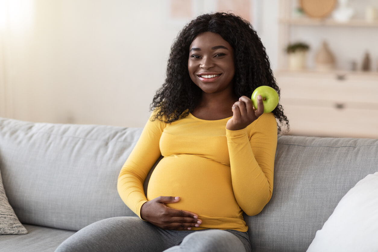 Mujer embarazada comiendo manzana durante el embarazo, uno de los alimentos fáciles de digerir.