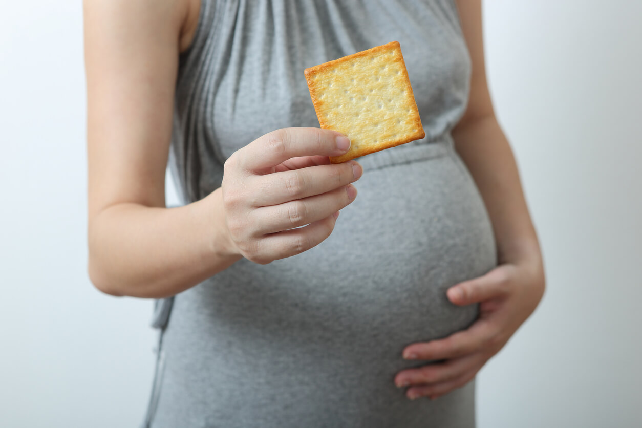 Femme enceinte mangeant un biscuit salé, l'un des remèdes naturels pour traiter les nausées matinales.