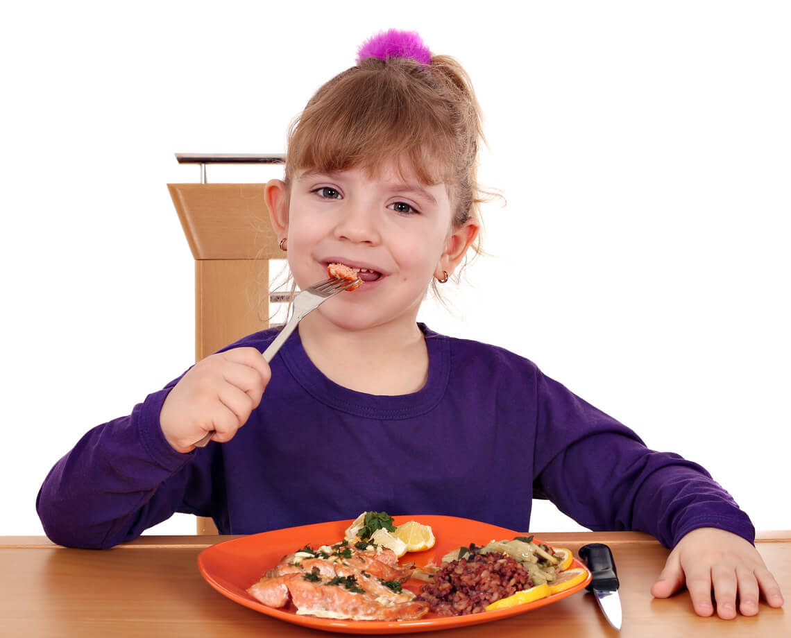 Niña comiendo salmón, uno de los alimentos que cuida el corazón del niño.