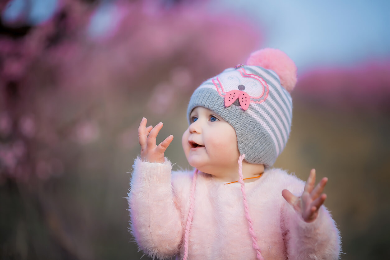 A baby wearing a knit hat and a fuzzy pink sweater outdoors.