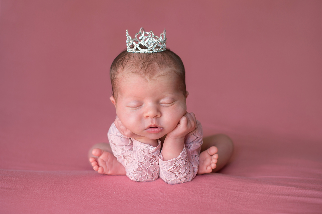 A newborn baby sleeping with a tiny crown on her head.