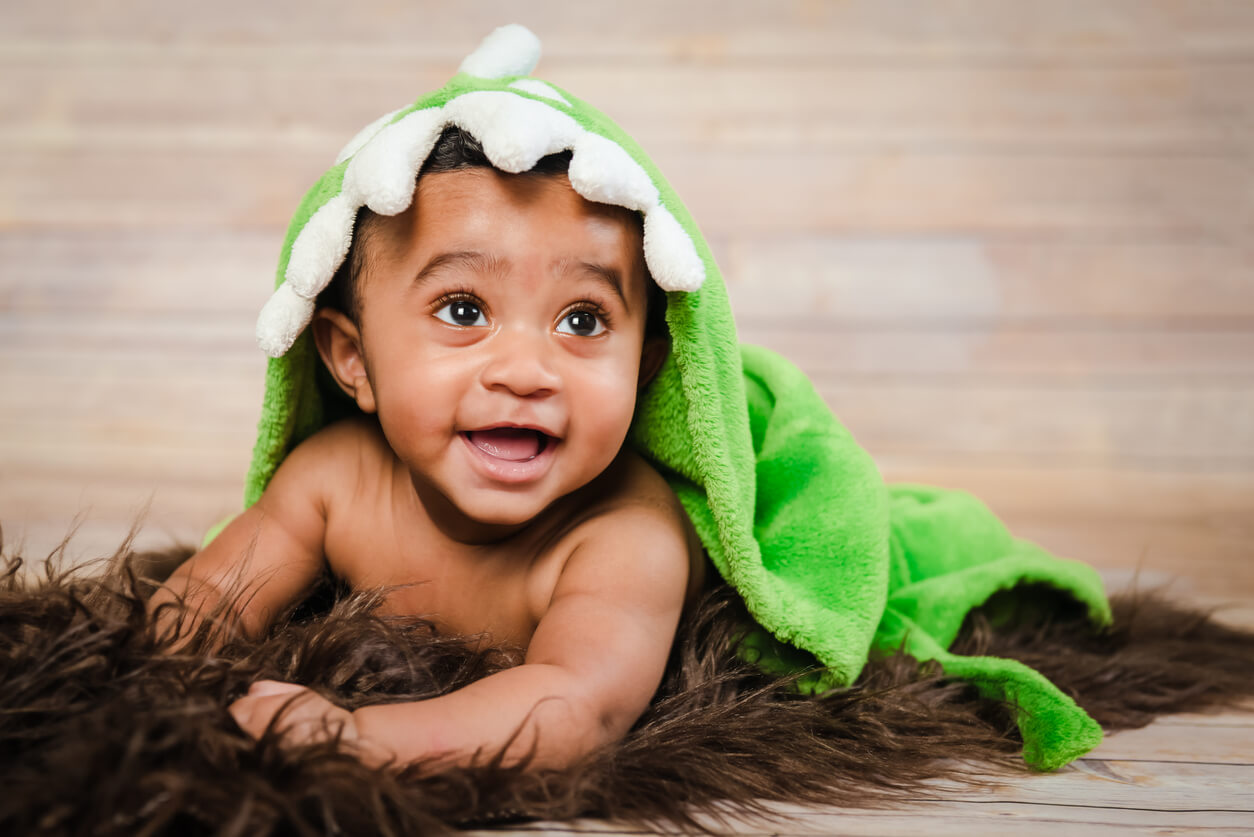 A baby bow with a dinasour blanket on top of him.