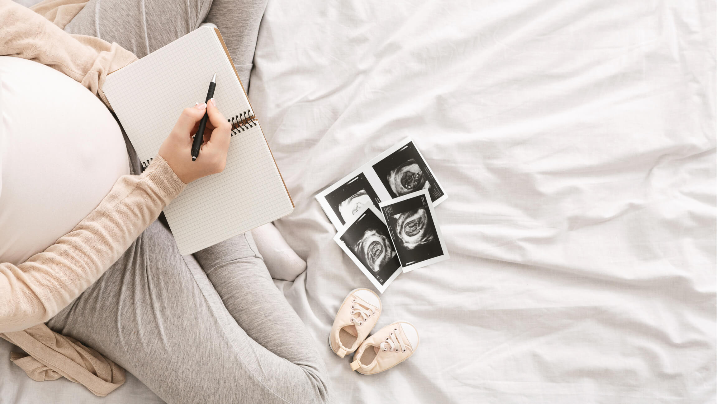 A pregnant woman looking at ultrasound pictures and writing in a notebook.