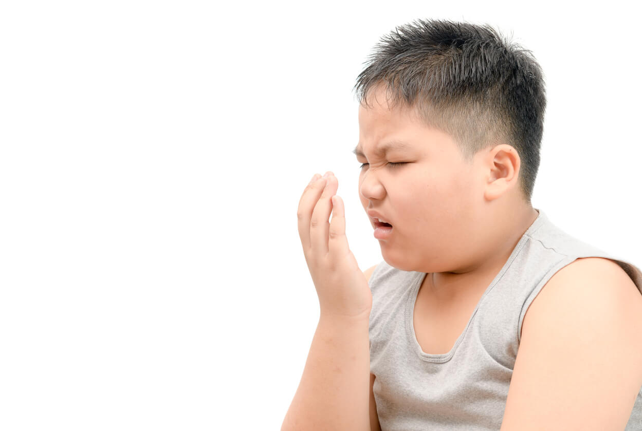 Un enfant en surpoids qui grimace avec une main devant sa bouche.