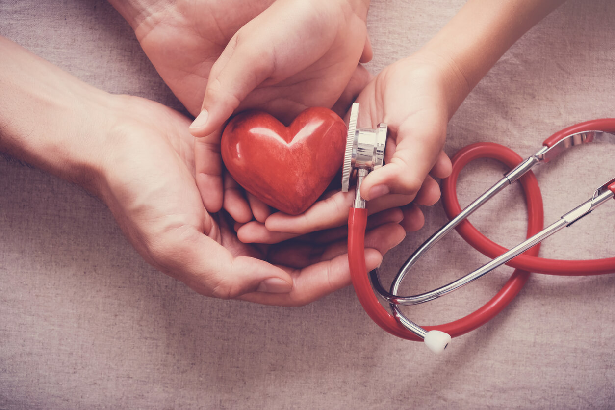 Quatre mains qui tiennent un stéthoscope avec un coeur.