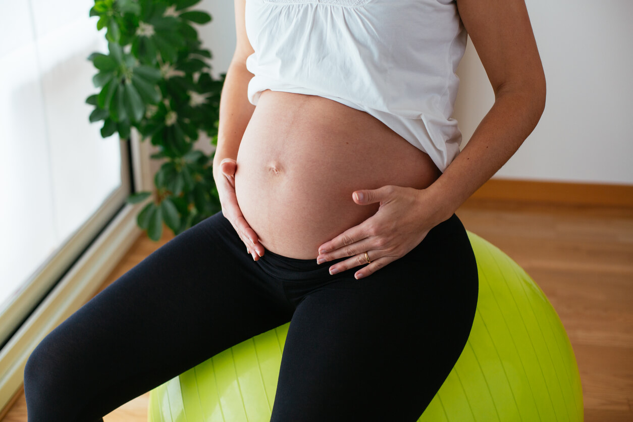 Une femme enceinte assise sur un ballon de gym. 