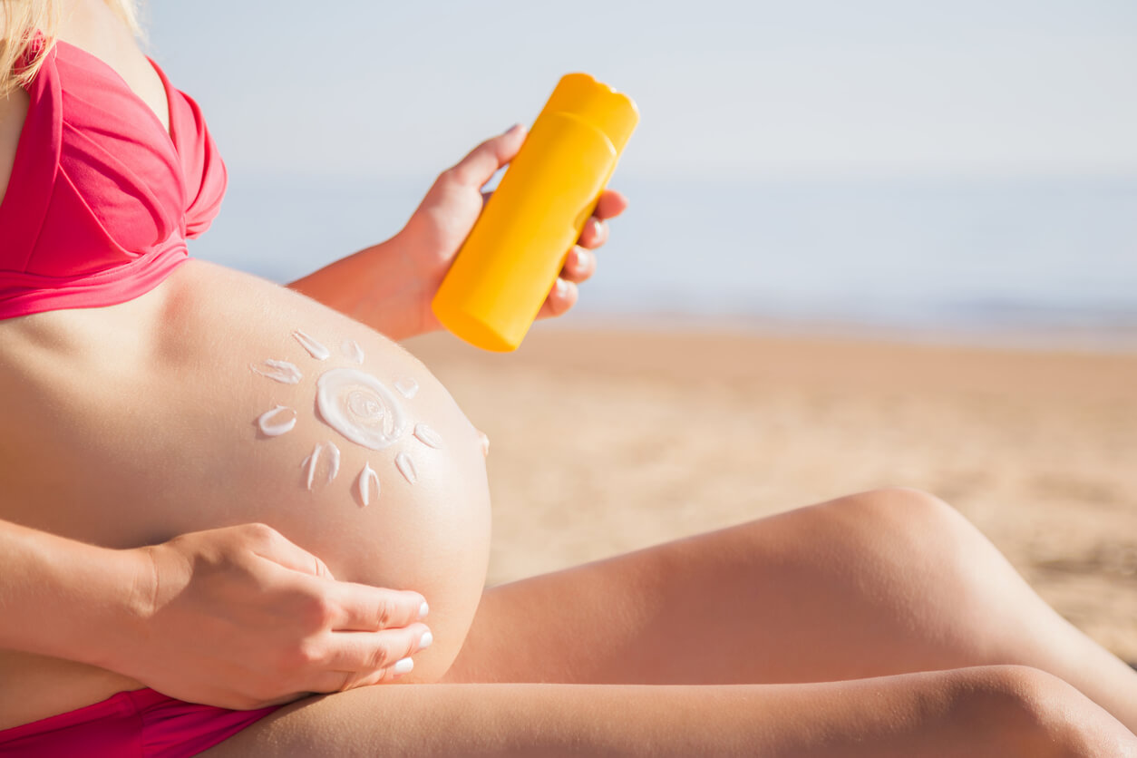 Gravid kvinne som bruker sikker solkrem på stranden.