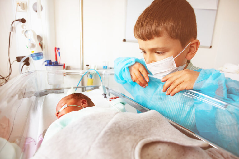 Un enfant masqué qui regarde un bébé prématuré dans sa couveuse. 
