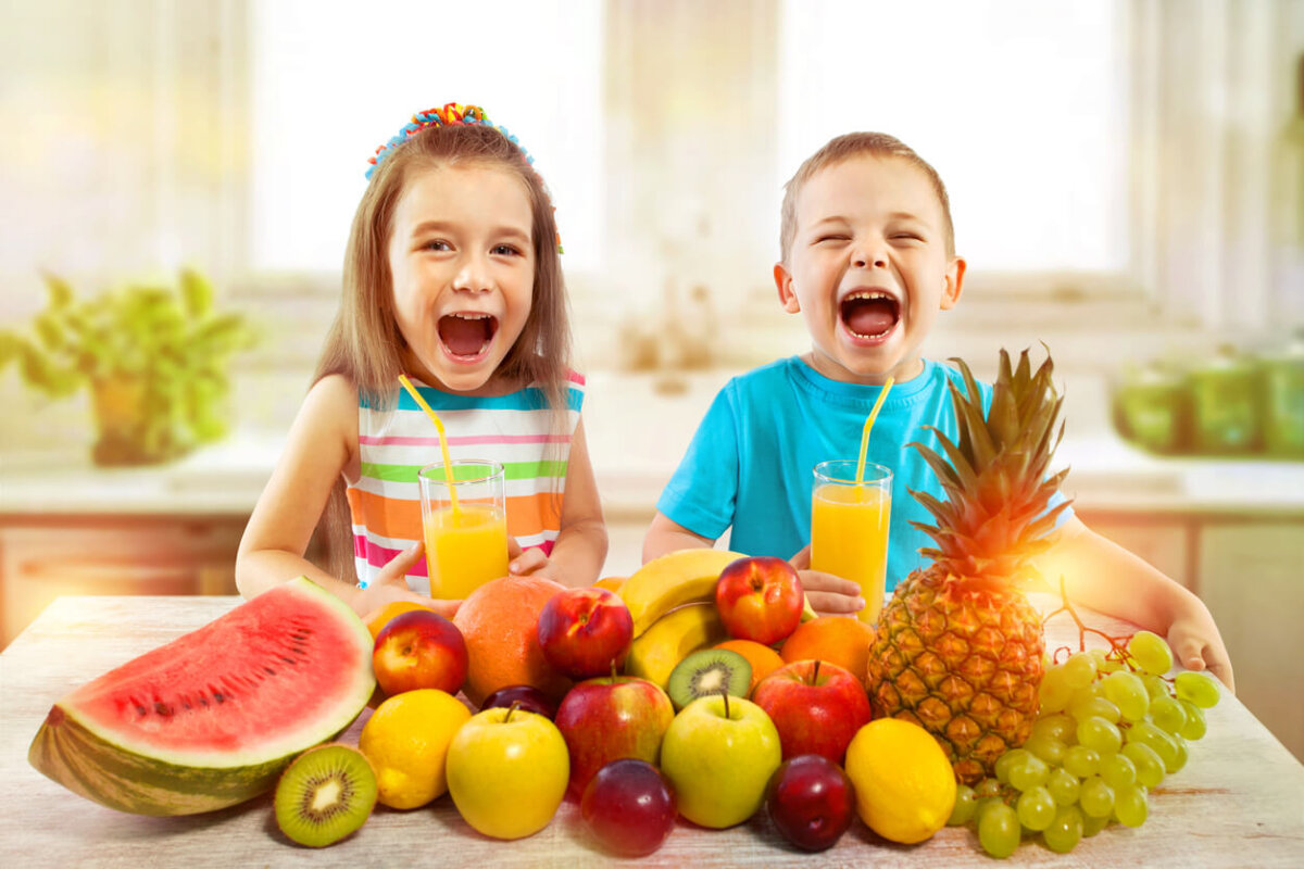 Niños rodeados de muchas frutas.