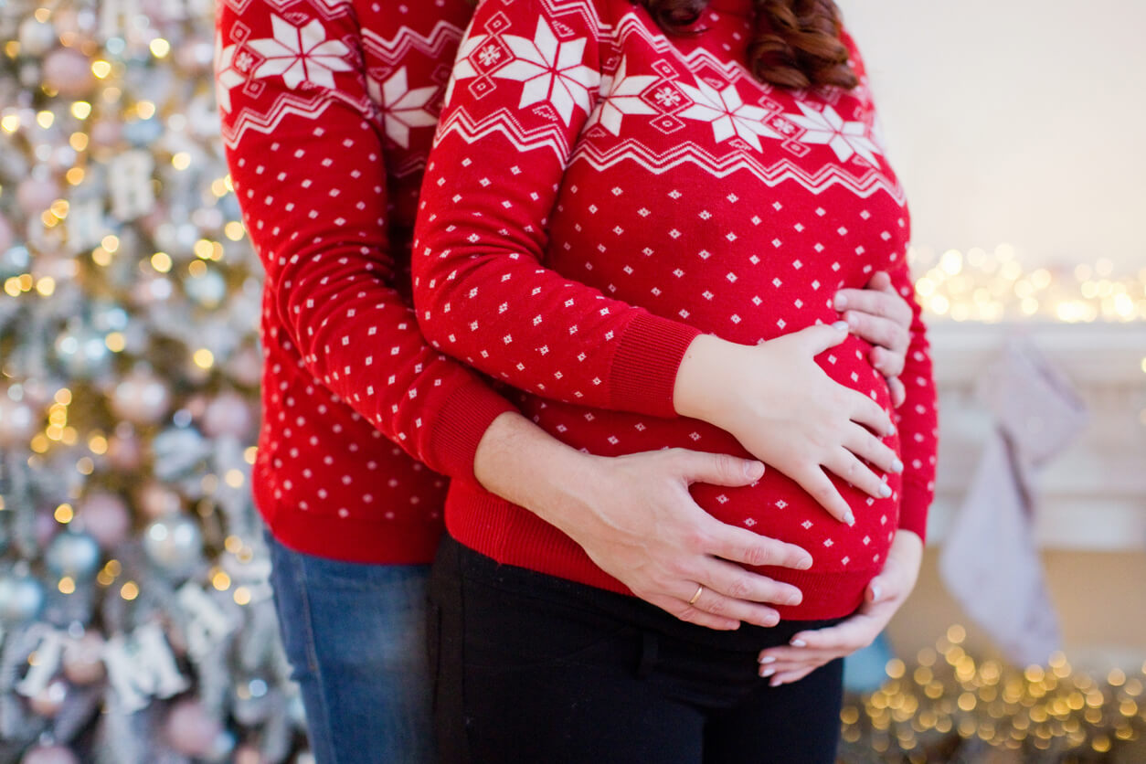 A pregnant couple wearing Christmas sweaters.