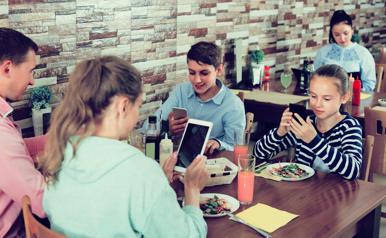 Het hele gezin in een restaurant met de telefoon in de hand
