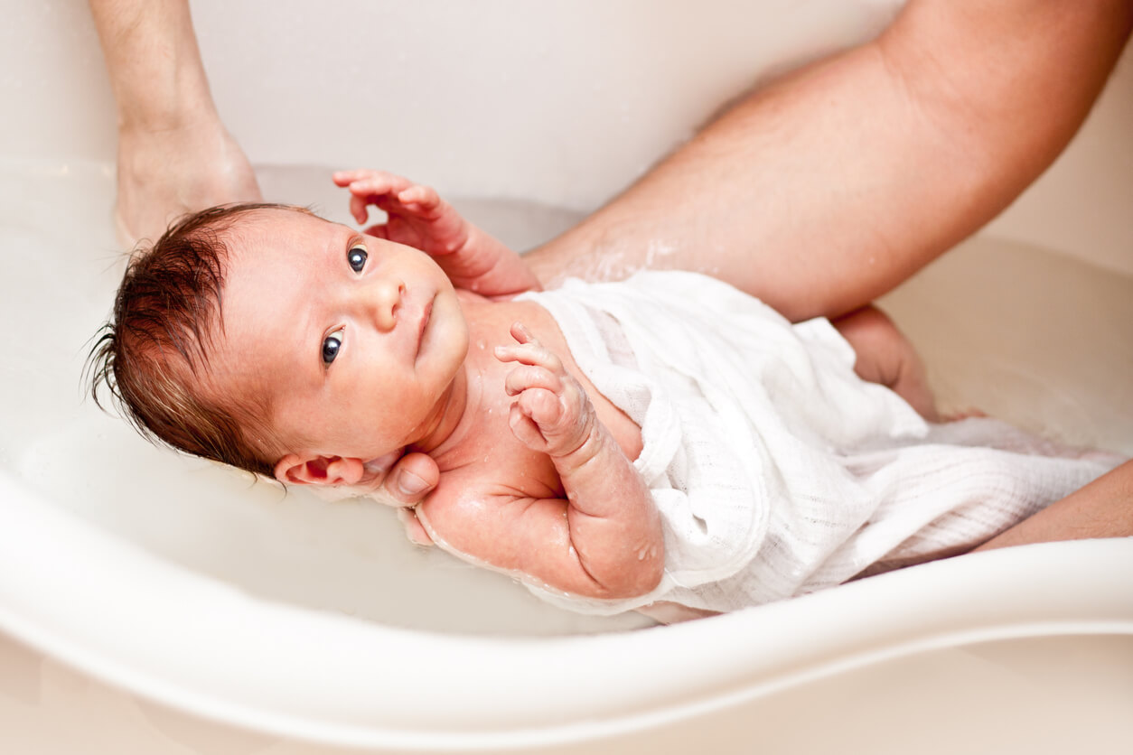 bano recien nacido neonato primer experiencia higiene cuerpo cordon cuidado bebe brazos padres banera agua
