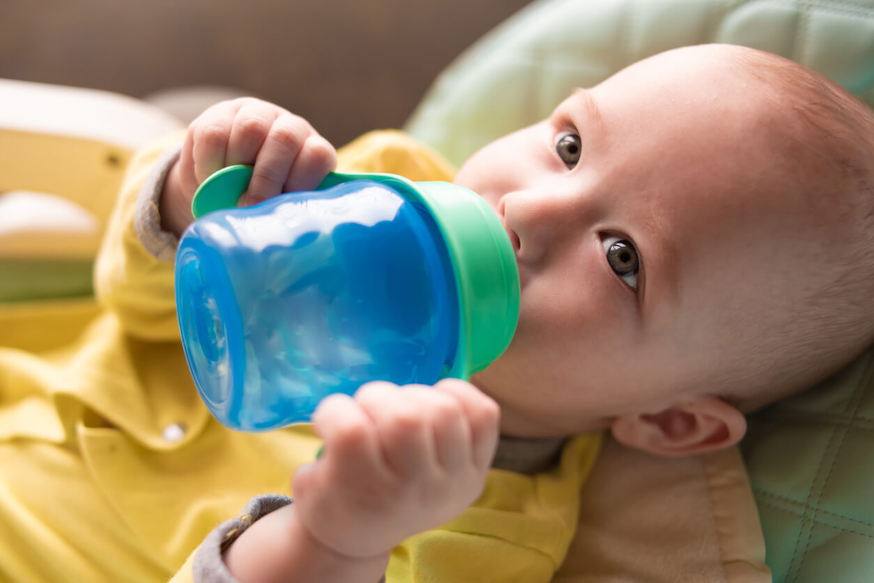 Un bébé qui boit dans une tasse avec des poignées. 