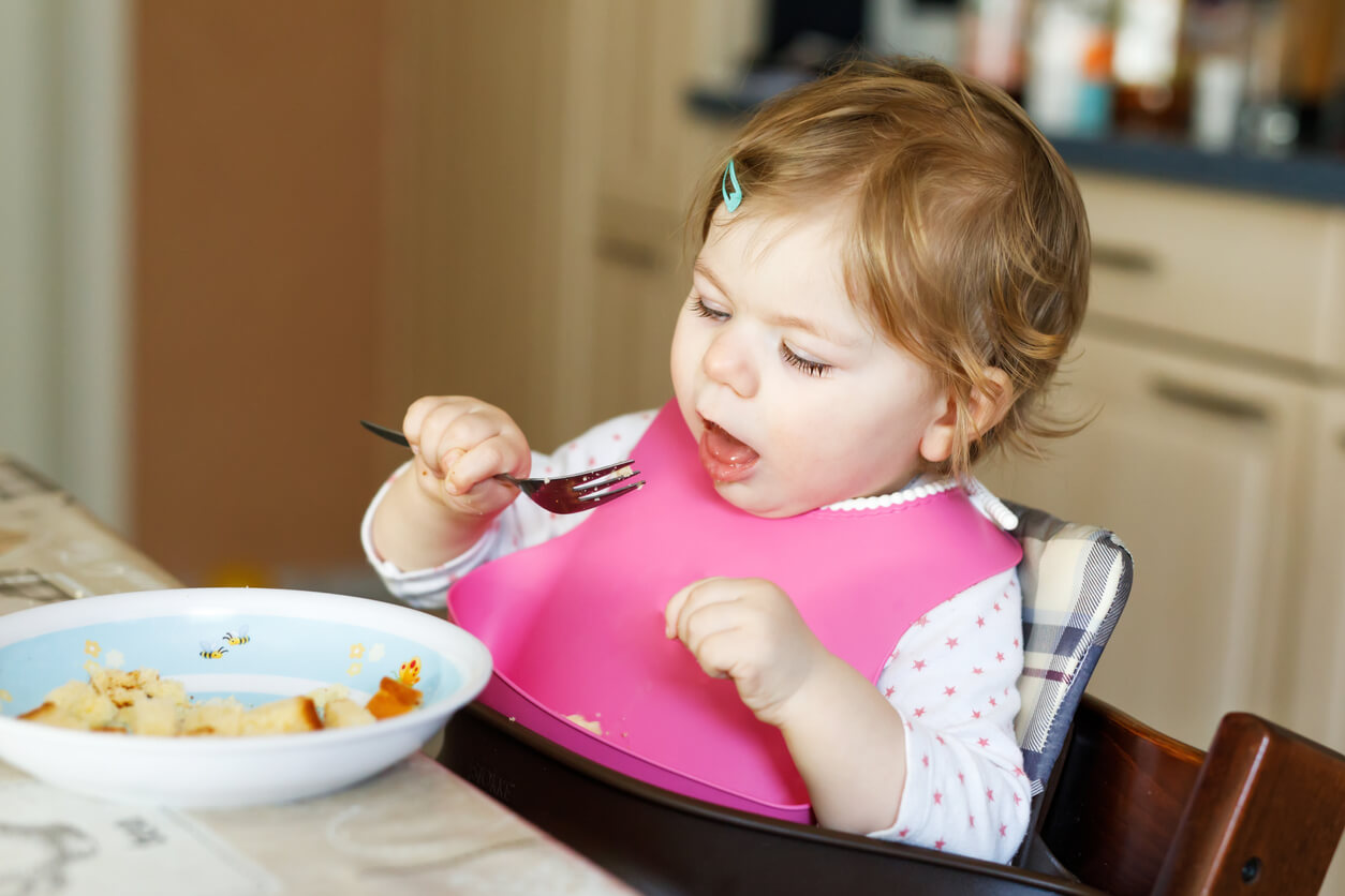 bebe nena nina comiendo sentada silla babero blw tenedor bliss comida alimento plato trozos aprendizaje