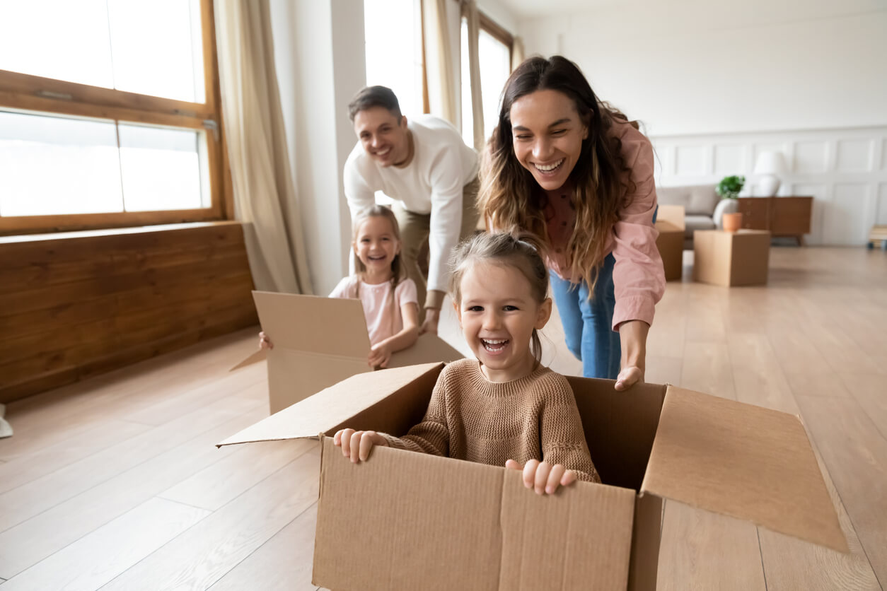 Parents pushing their daughters around the house in cardboard boxes.
