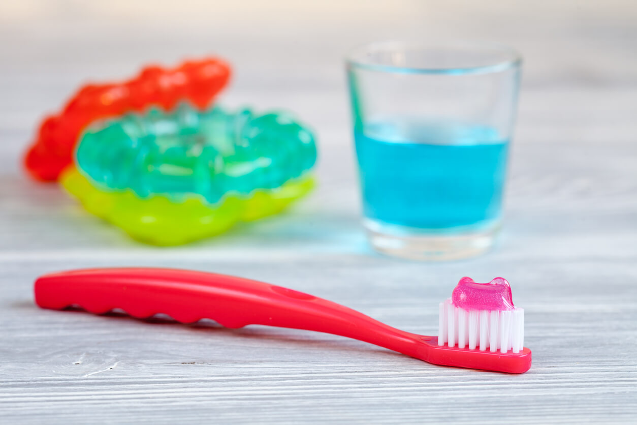 A baby's toothbrush, teethers, and a cup of fluoride rinse.