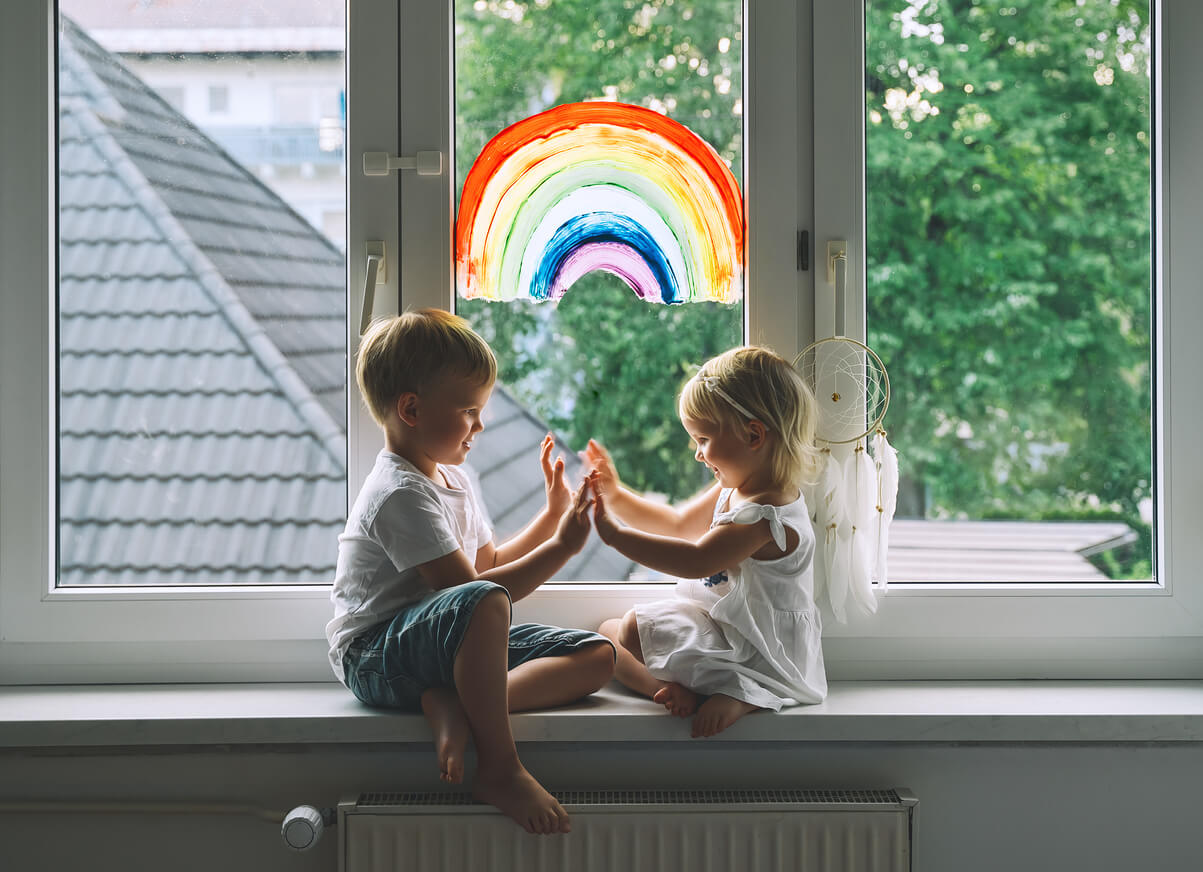 Children playing patty cake in front of a decorated window.