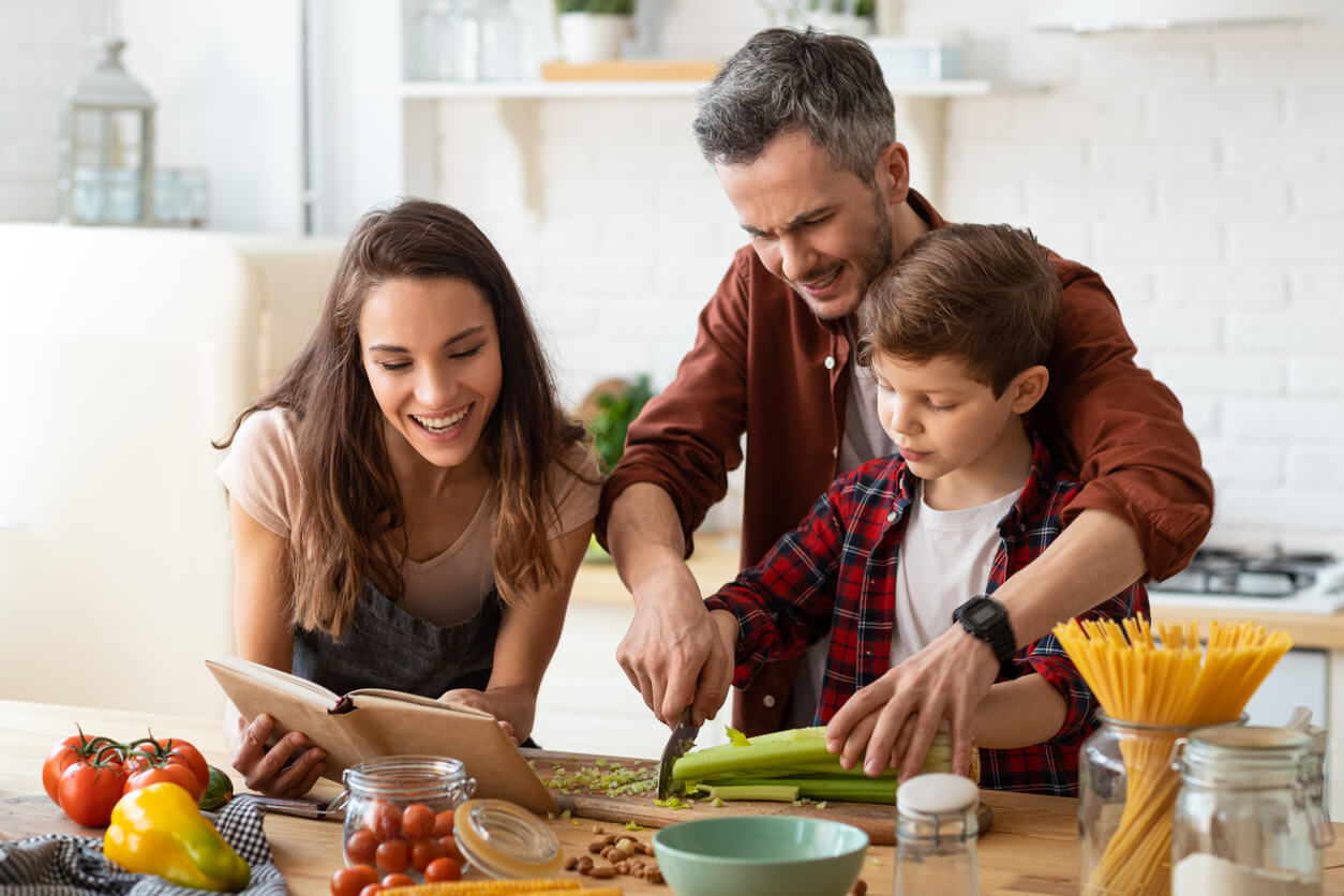 pai mãe ensina filho filho corta legumes mesada de cozinha lição de autonomia pais aprendizagem ajuda