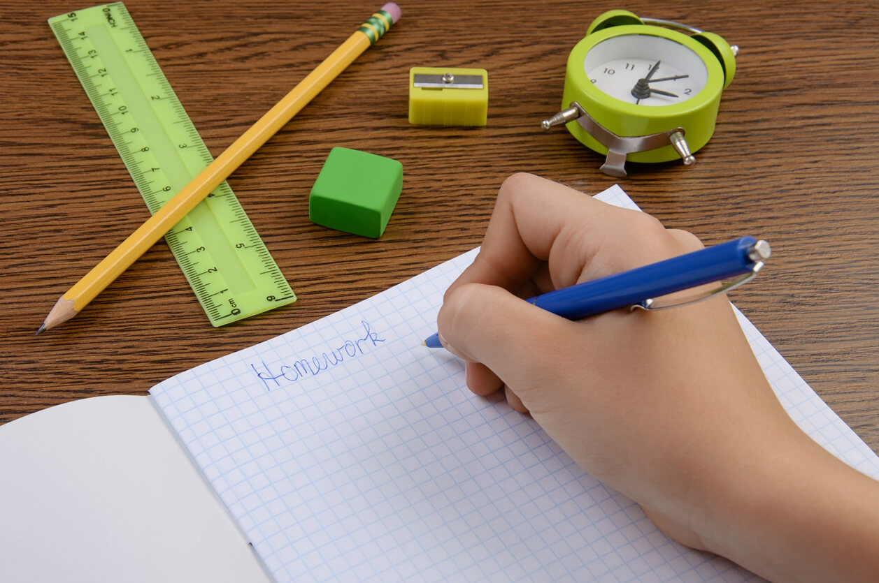 La main d'un enfant qui fait ses devoirs avec un cahier, une règle et des crayons.