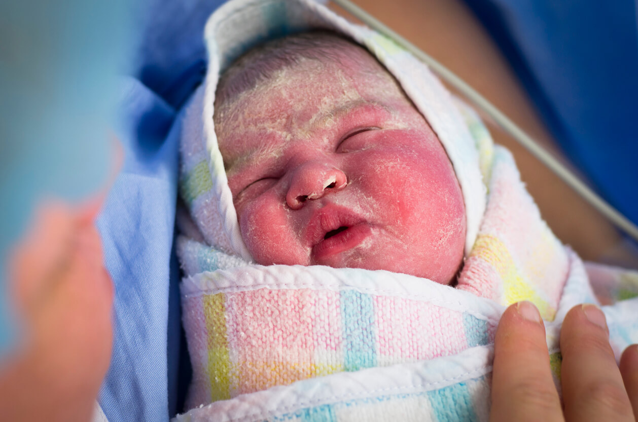 Un nouveau-né enveloppé dans une serviette avec des restes de vernix caseosa sur la peau. 
