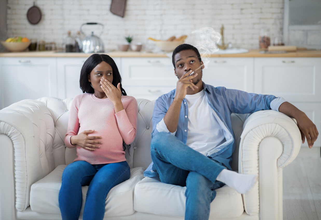 Une femme enceinte assise à côté de son mari qui fume. 