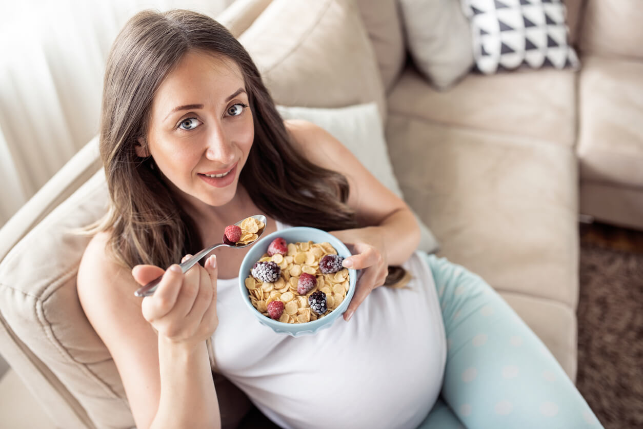 embarazada mujer come tazon cereales frutas fibra carbohidratos complejos desayuno merienda sillon dia dieta saludable prevencion enfermedad metabolica