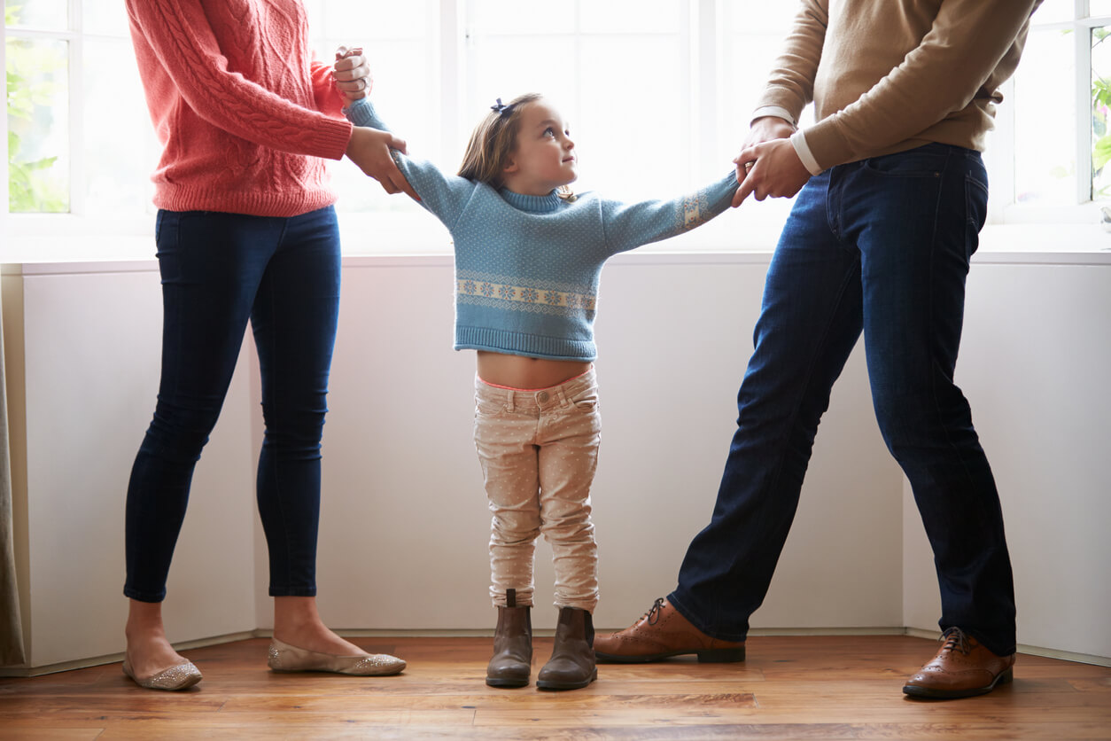 Une jeune fille prise par les bras par ses deux parents. 