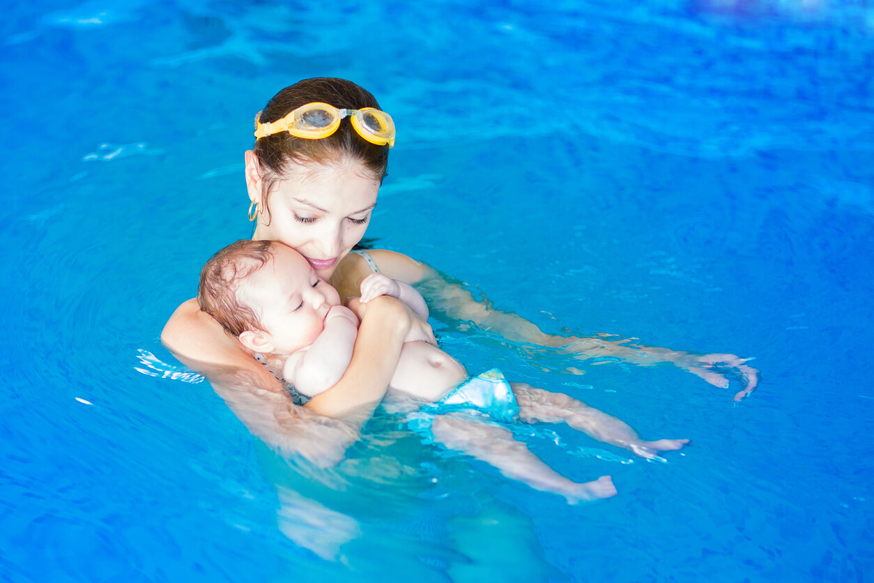 A mother swimming in a pool with her tiny baby.