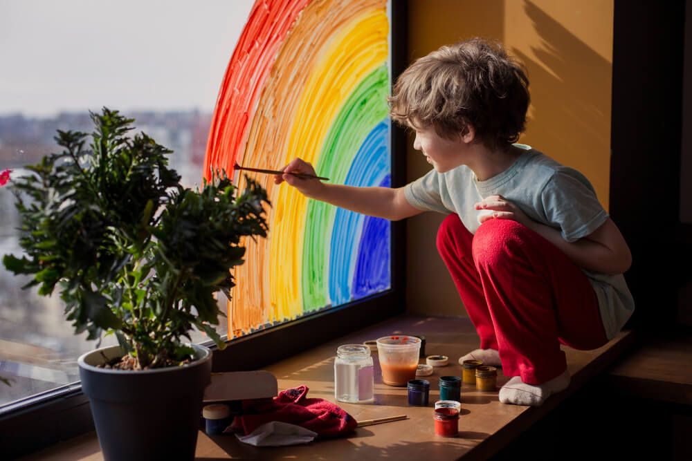 Un enfant qui dessine un arc-en-ciel sur une fenêtre.