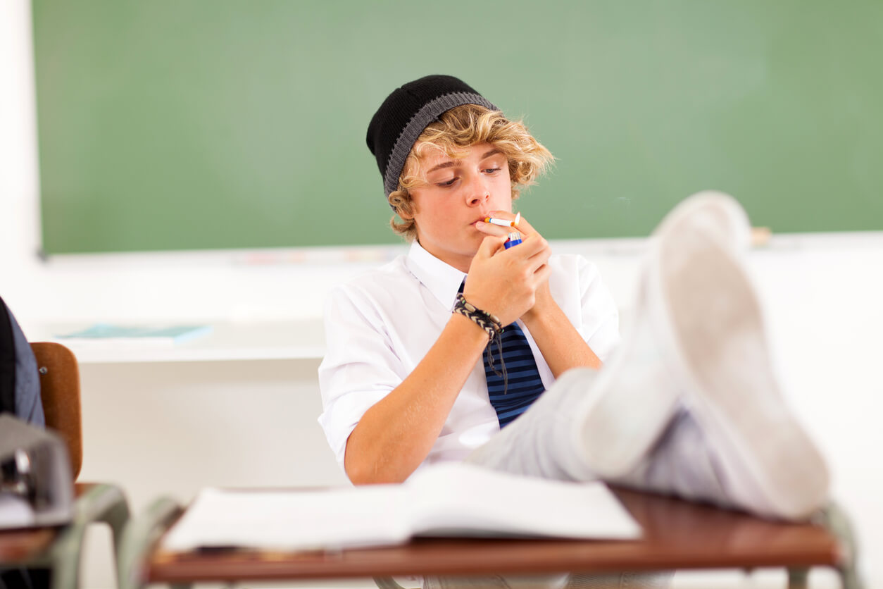A teen lighting a cigarette at his desk.