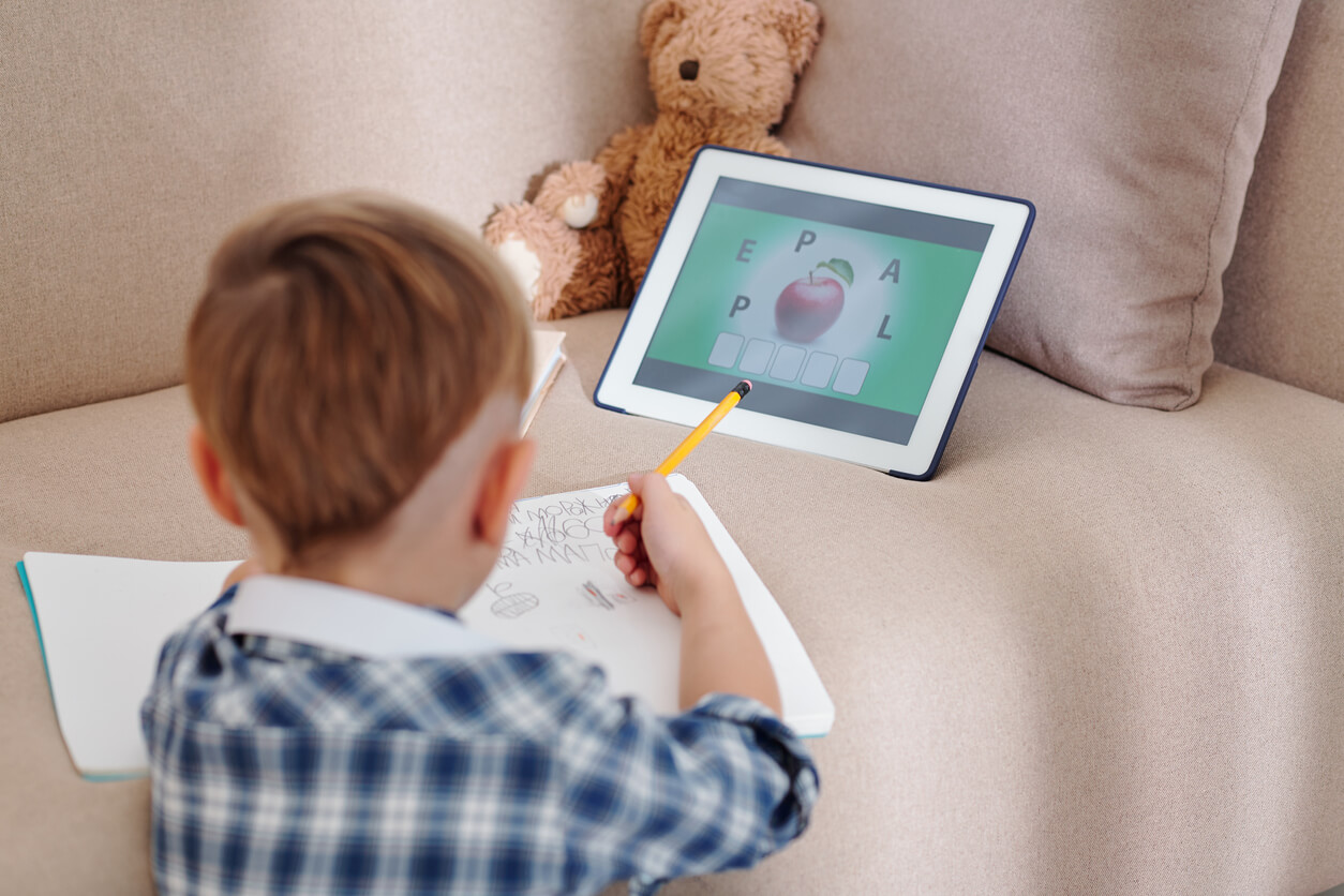 nino escolar aprende lenguaje escritura lectura en casa sillon tablt oso de felpa cuaderno lapiz escribe copia