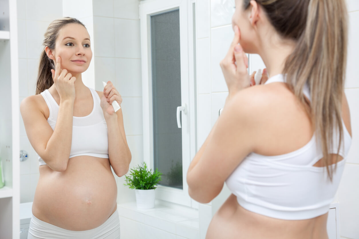 A pregnant woman putting cream on her face.