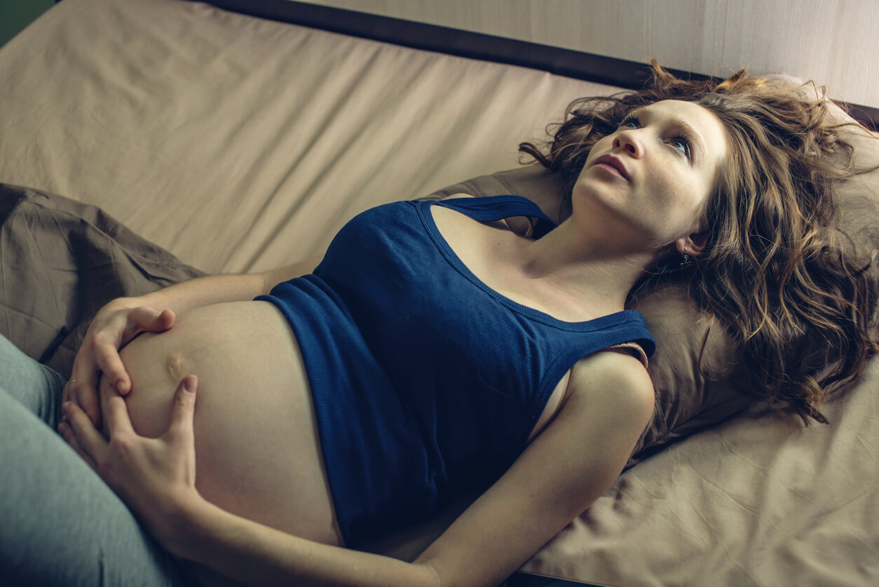 Une femme enceinte pensive et allongée.