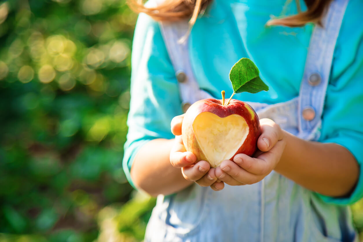 A girl holding an apple with a heart shape cut out of it.