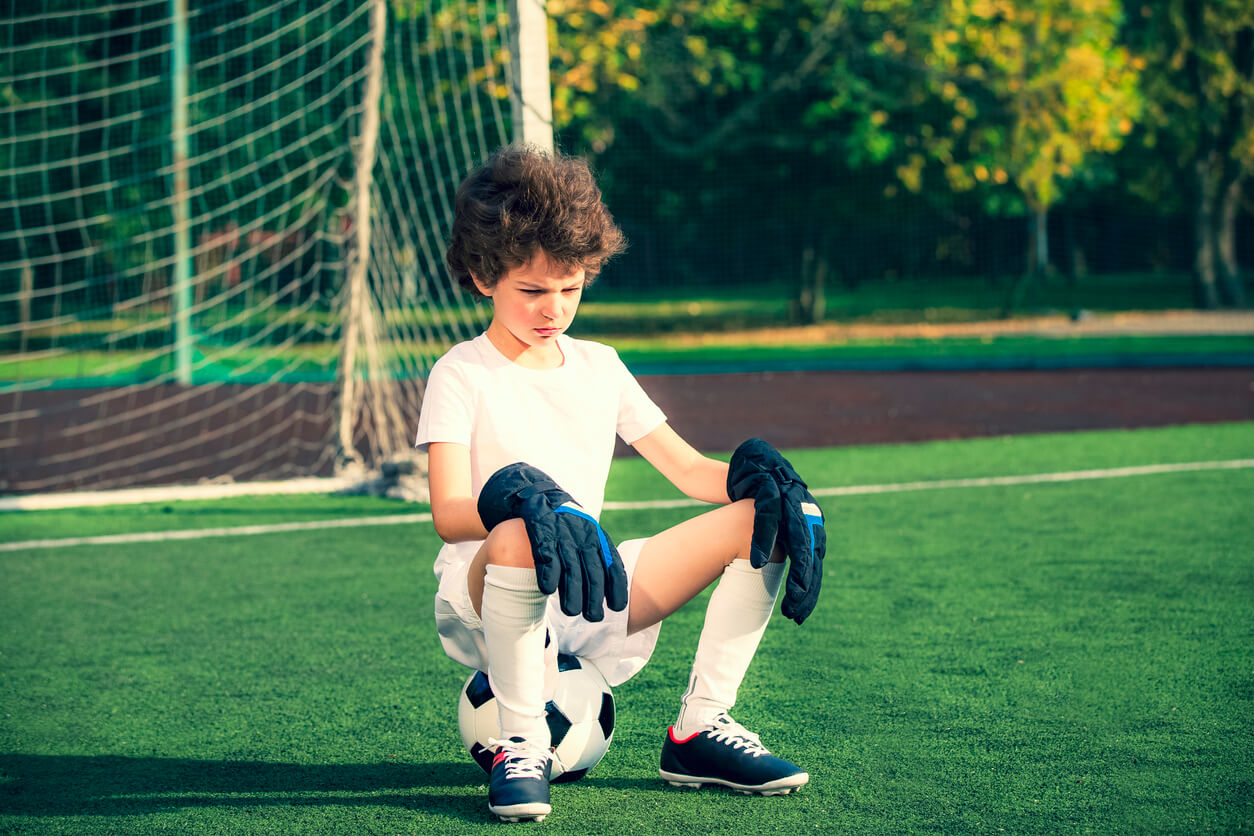An angry child sitting on a soccer ball on a soccer field.