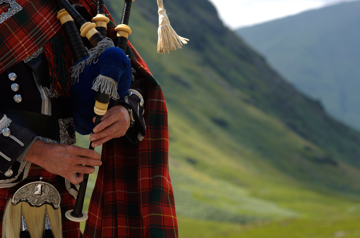 A man playing the bagpipes in the hills of Scotland.